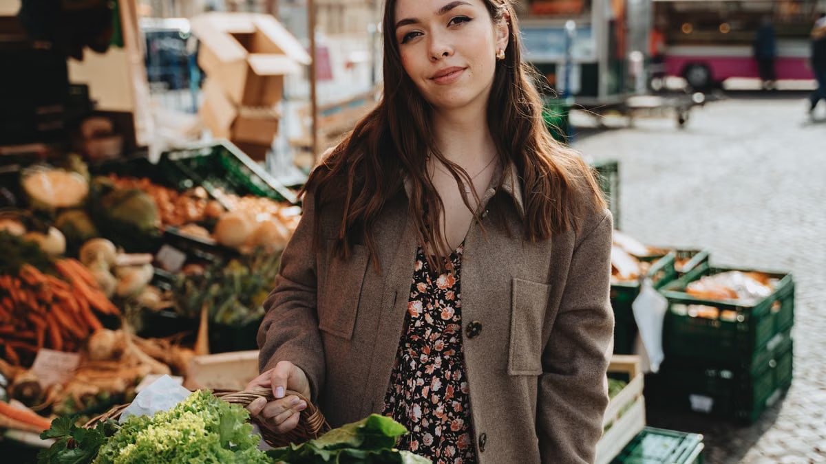Woman buying fresh produce at an outdoor market in Erfurt, Germany with a basket of vegetables.