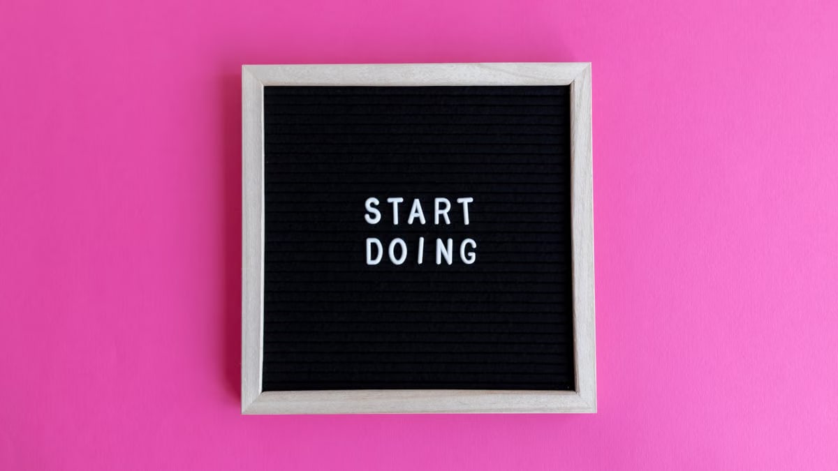 Black letter board with 'Start Doing' motivational text on bright pink background.